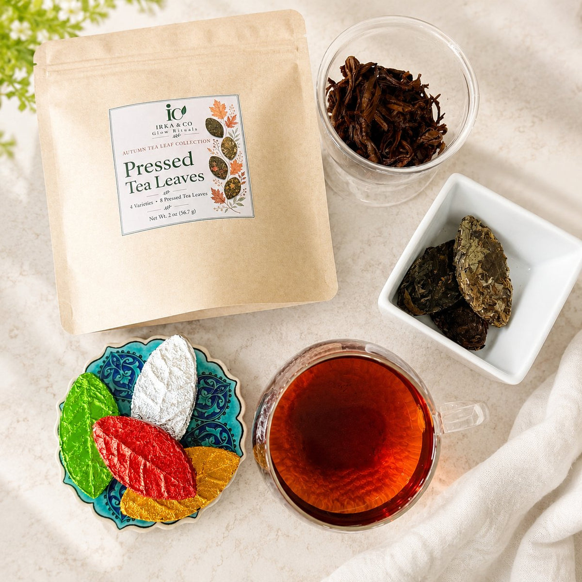 Pressed Tea Leaves kraft pouch with a cup of dark brewed tea, loose tea leaves and colorful leaf-shaped teas on a blue coaster