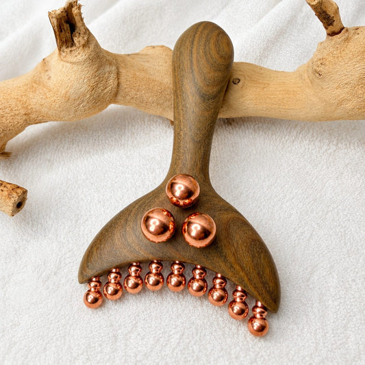 Copper & Wood Deep Tissue Massage Tool styled resting on a driftwood branch against a white textured cloth, showing the full copper ball layout
