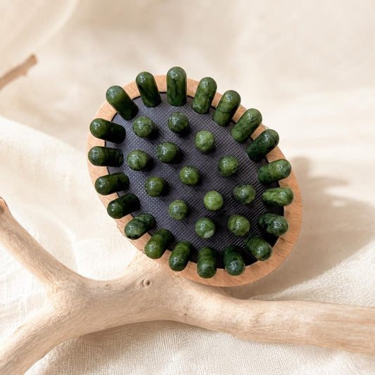 Top-down close-up of the Jade Lymphatic Massage Brush showing all polished jade nodes, resting on cream cloth with driftwood