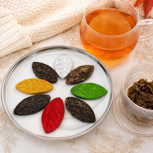 Autumn pressed tea leaves on a plate with a cup of freshly brewed amber tea and opened tea leaves in a glass
