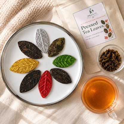 Pressed tea leaves in fall colors on a white plate with the Irka & Co pouch, an autumn maple leaf and a cup of tea