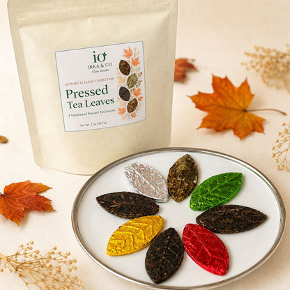 Close view of eight pressed tea leaves — white tea, raw pu-erh and black tea — shaped like autumn leaves on a plate