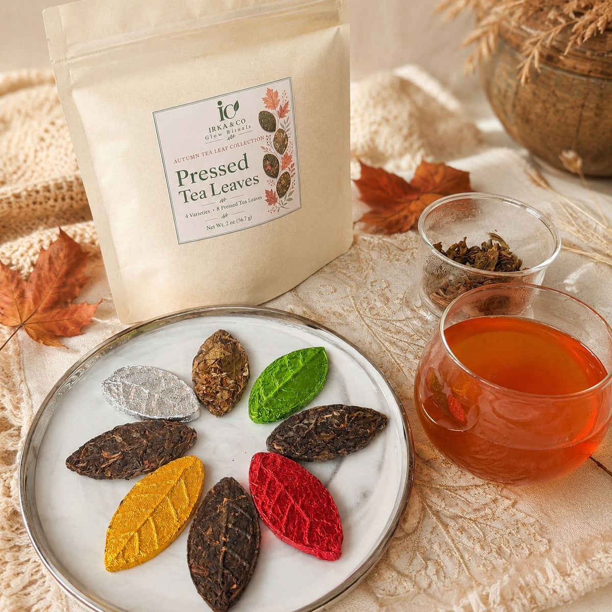 Autumn tea gift set styled with the pouch, brewed tea, opened tea leaves and fall leaves on a cozy cream background