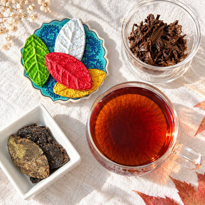 Pressed tea leaves in bright colors on a blue coaster beside a cup of dark brewed tea and compressed tea leaves in a white bowl
