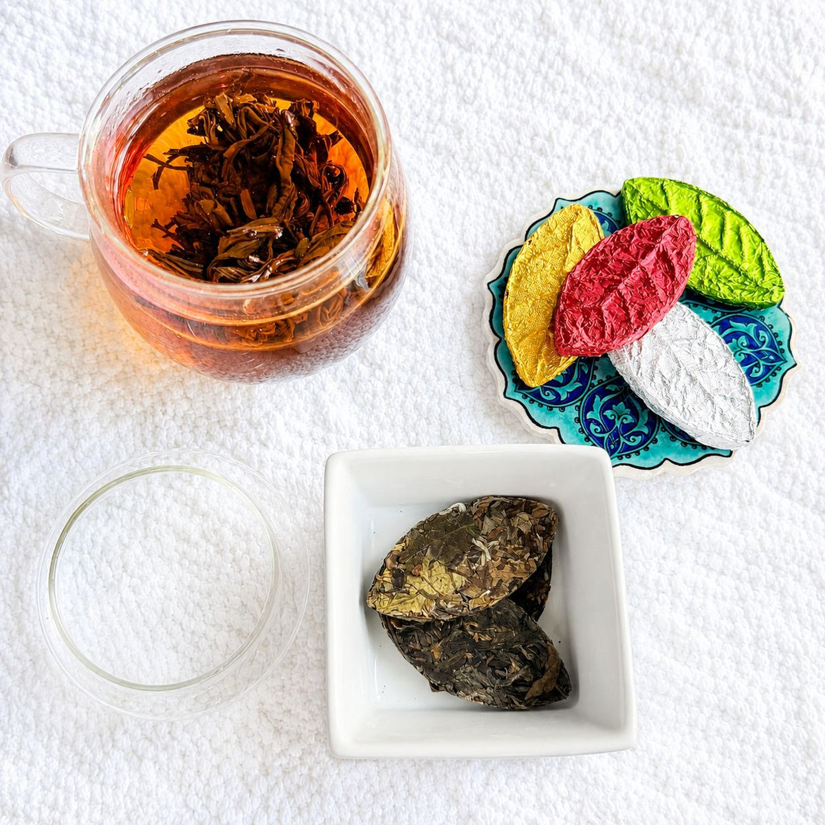 Glass cup of dark amber tea seen from above with colorful pressed tea leaves and dark tea leaves in a dish