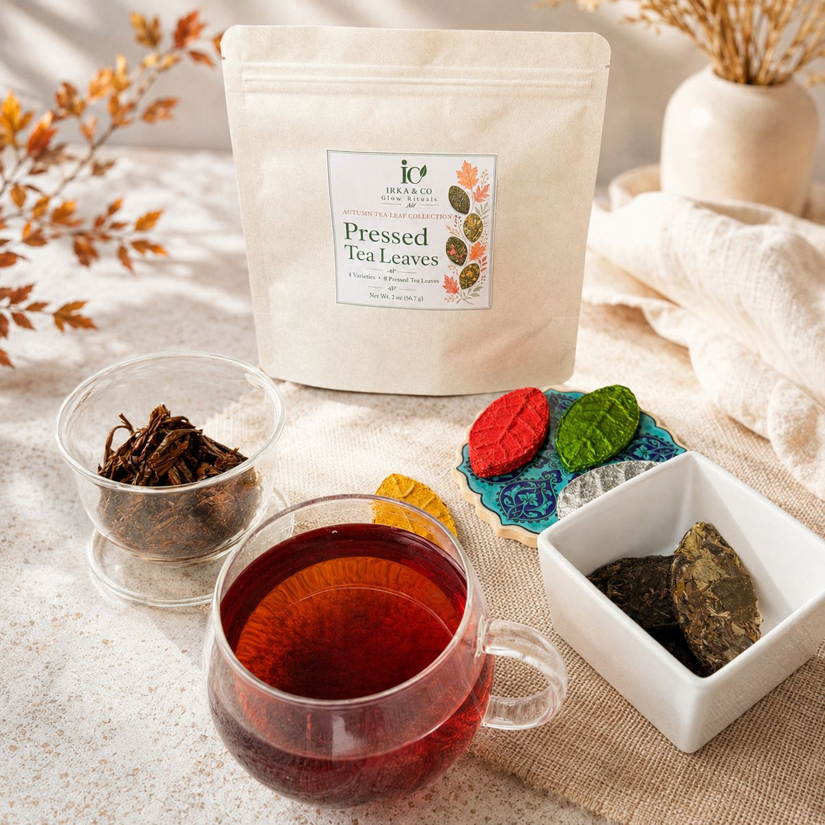 Kraft pouch of pressed tea leaves with a glass cup of brewed tea and colorful leaf-shaped teas on an autumn table