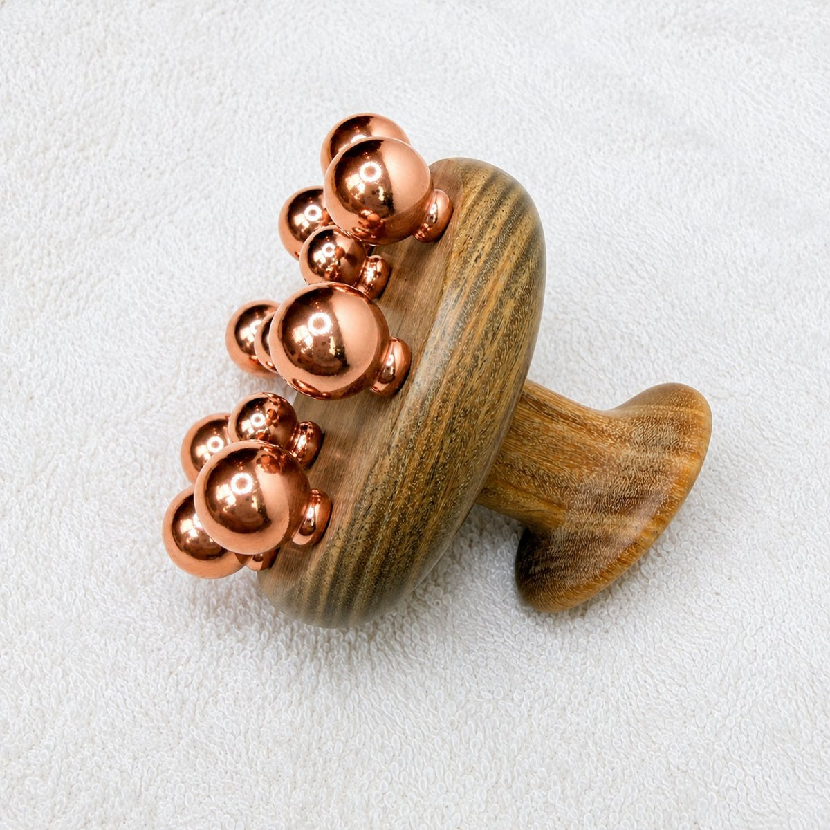 Copper cluster scalp and neck massage tool with green sandalwood mushroom-shaped handle on a white towel