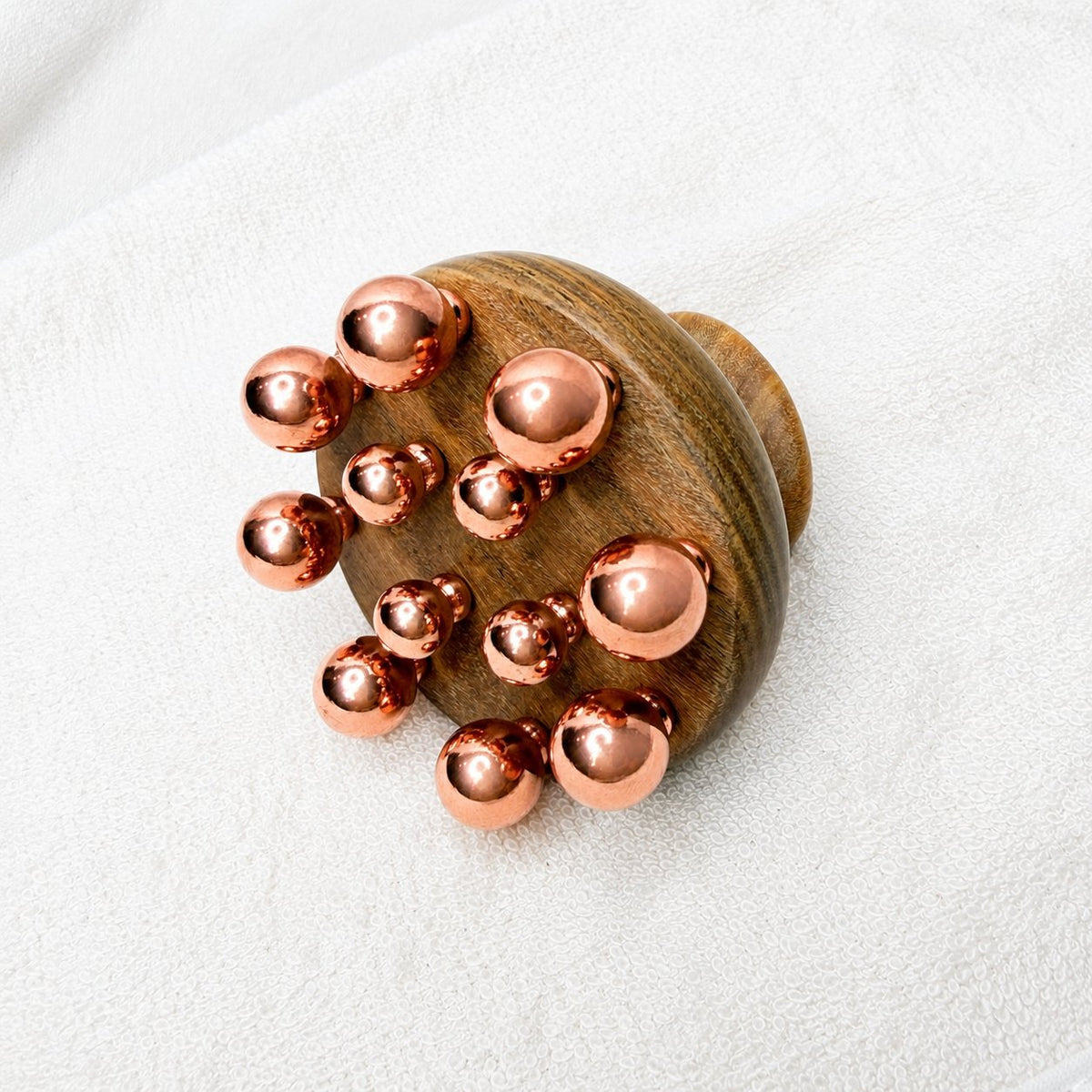 Front view of the copper cluster massage tool showing the graduated copper balls set into the wood