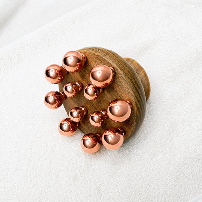 Front view of the copper cluster massage tool showing the graduated copper balls set into the wood