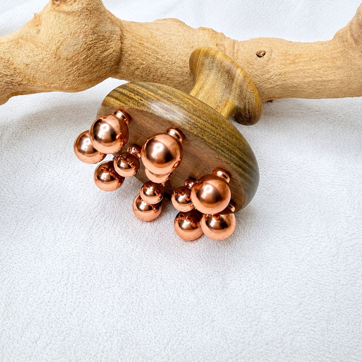 Copper cluster scalp and neck massage tool propped against driftwood on a white textured background