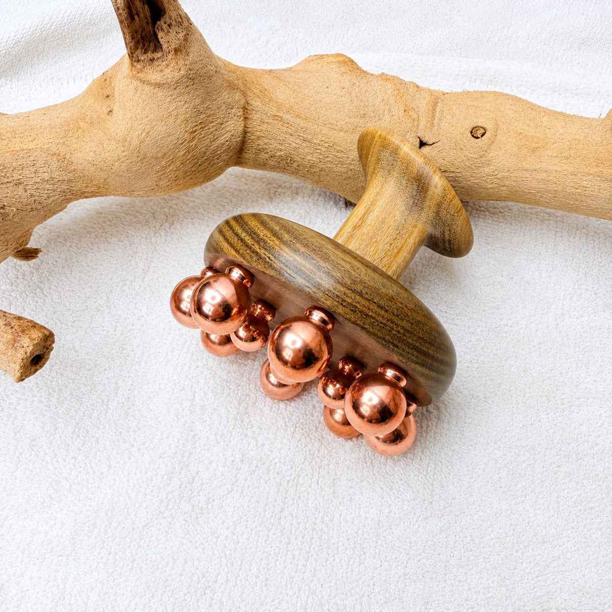 Copper cluster massage tool leaning on driftwood, side angle showing the sandalwood handle