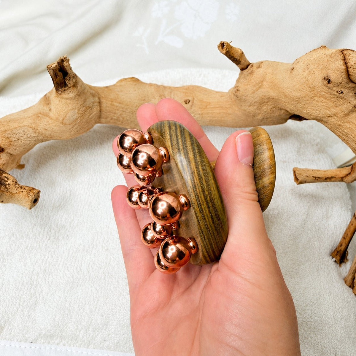 Copper cluster massage tool cupped in hand, showing how the copper balls fit against the palm