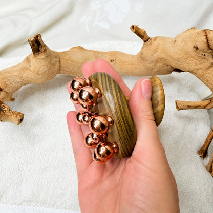 Copper cluster massage tool cupped in hand, showing how the copper balls fit against the palm
