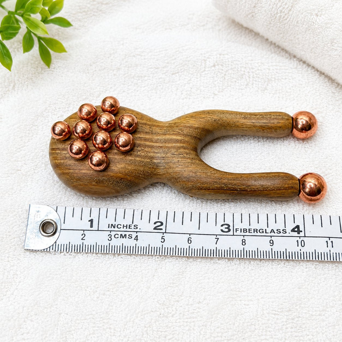 Copper and green sandalwood facial sculpting tool lying flat beside a ruler showing its 1.5 inch width