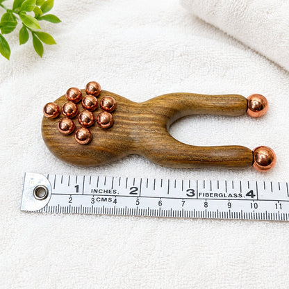 Copper and green sandalwood facial sculpting tool lying flat beside a ruler showing its 1.5 inch width