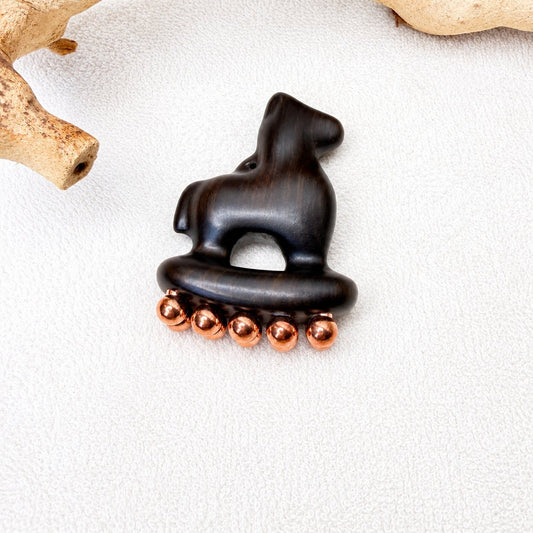Copper & Purple Sandalwood Little Horse facial massage tool resting on driftwood against a white textured background