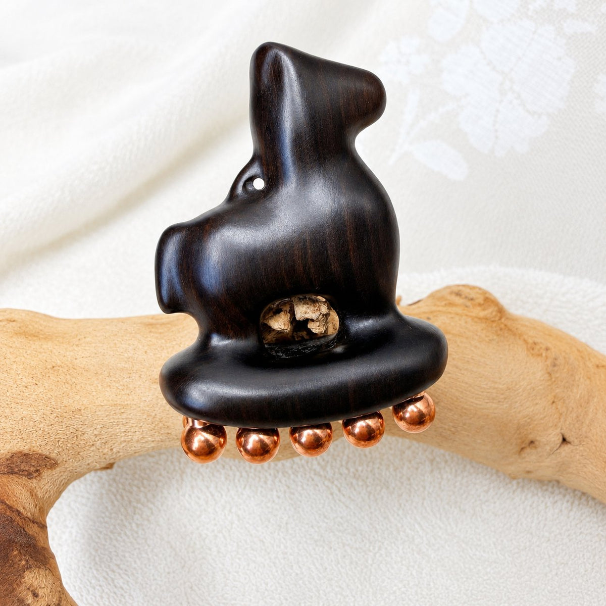 Little Horse facial massage tool resting on a driftwood branch, showing the carved finger-rest opening and copper balls