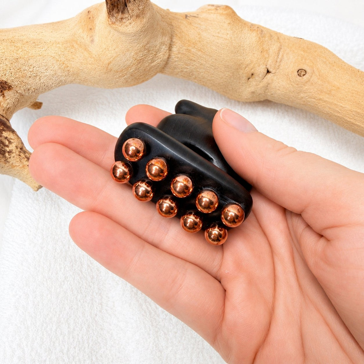 Underside of the Little Horse facial tool held in hand, showing the ten rounded copper massage balls