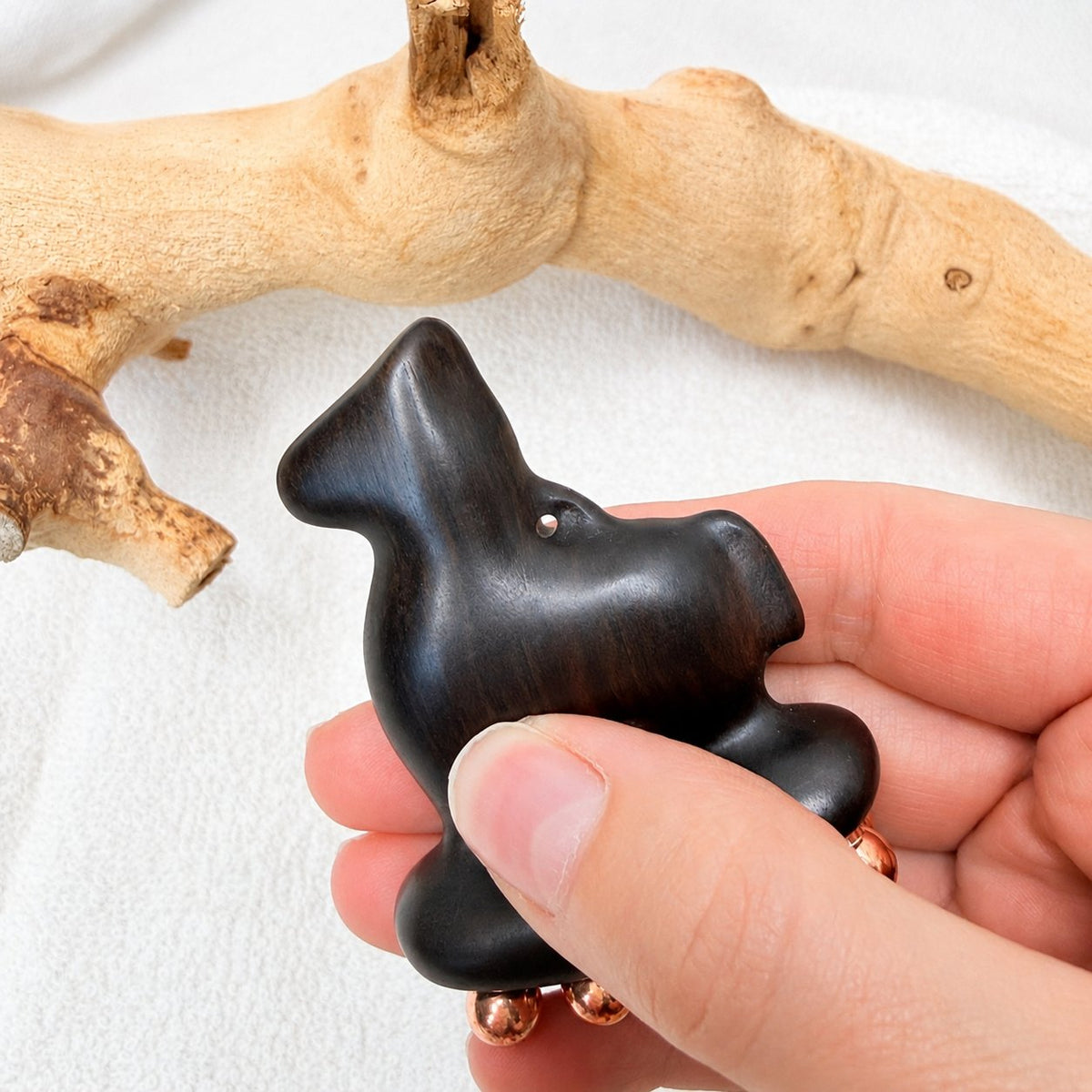 Little Horse facial massage tool held between two fingers, showing the purple sandalwood grain