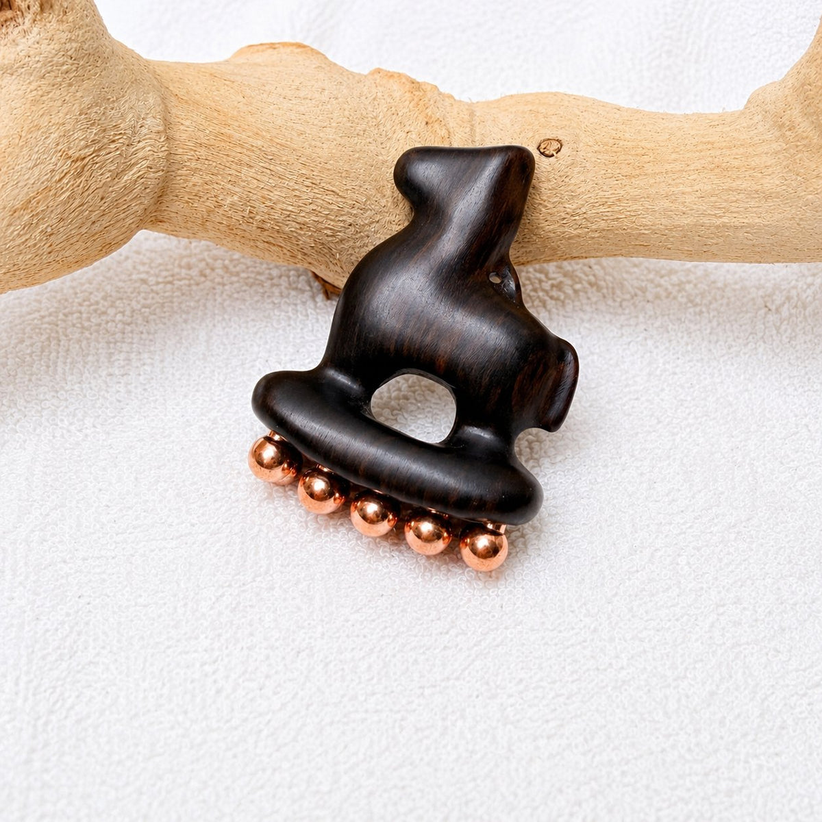 Copper and purple sandalwood Little Horse facial tool propped against driftwood, side angle