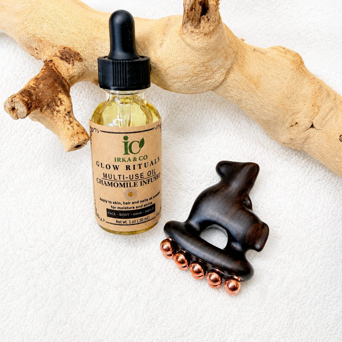 Copper and purple sandalwood facial tool and Glow Rituals botanical oil bottle displayed together on driftwood