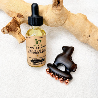 Copper and purple sandalwood facial tool and Glow Rituals botanical oil bottle displayed together on driftwood