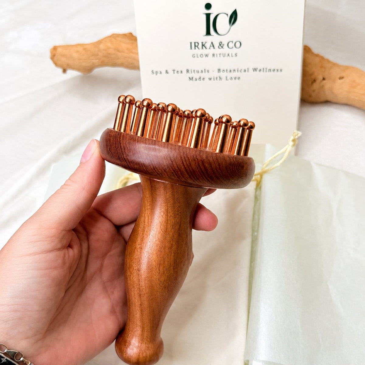 Copper & Rosewood Deep Tissue Massager held in hand with the Irka & Co Glow Rituals gift card behind it
