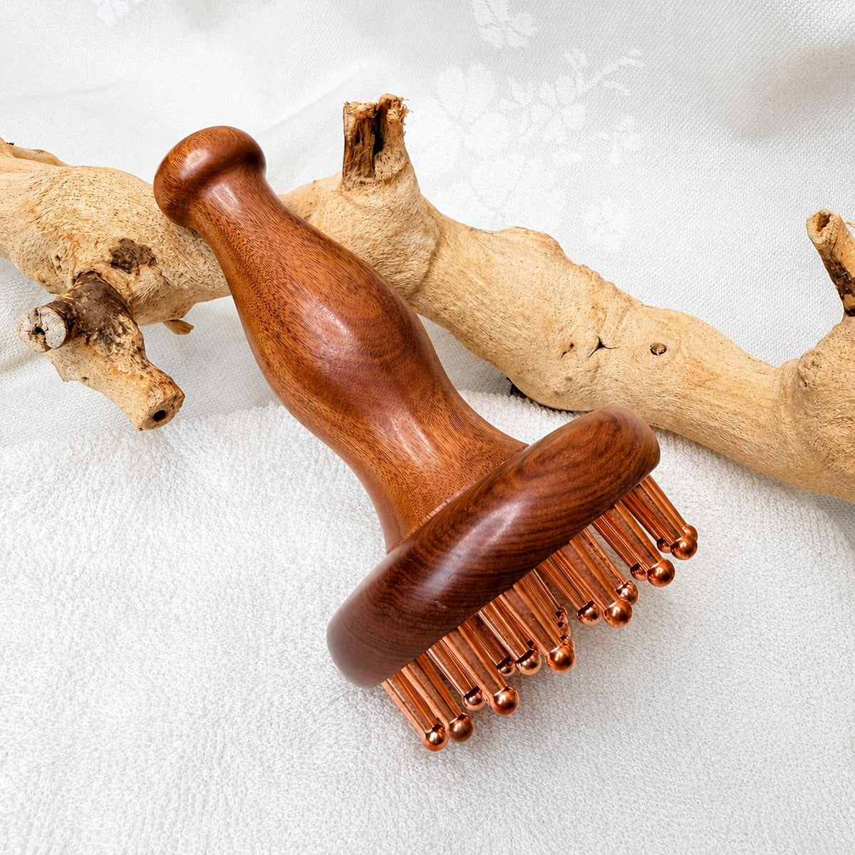 Copper & Rosewood Deep Tissue Massager propped against driftwood on a white textured background