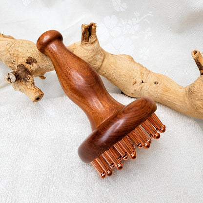Copper & Rosewood Deep Tissue Massager propped against driftwood on a white textured background