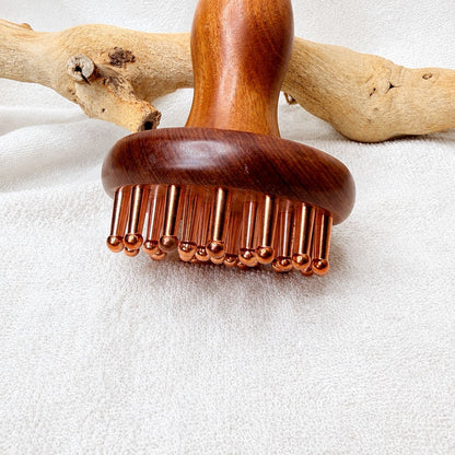 Front view of the Copper & Rosewood Deep Tissue Massager standing upright against driftwood