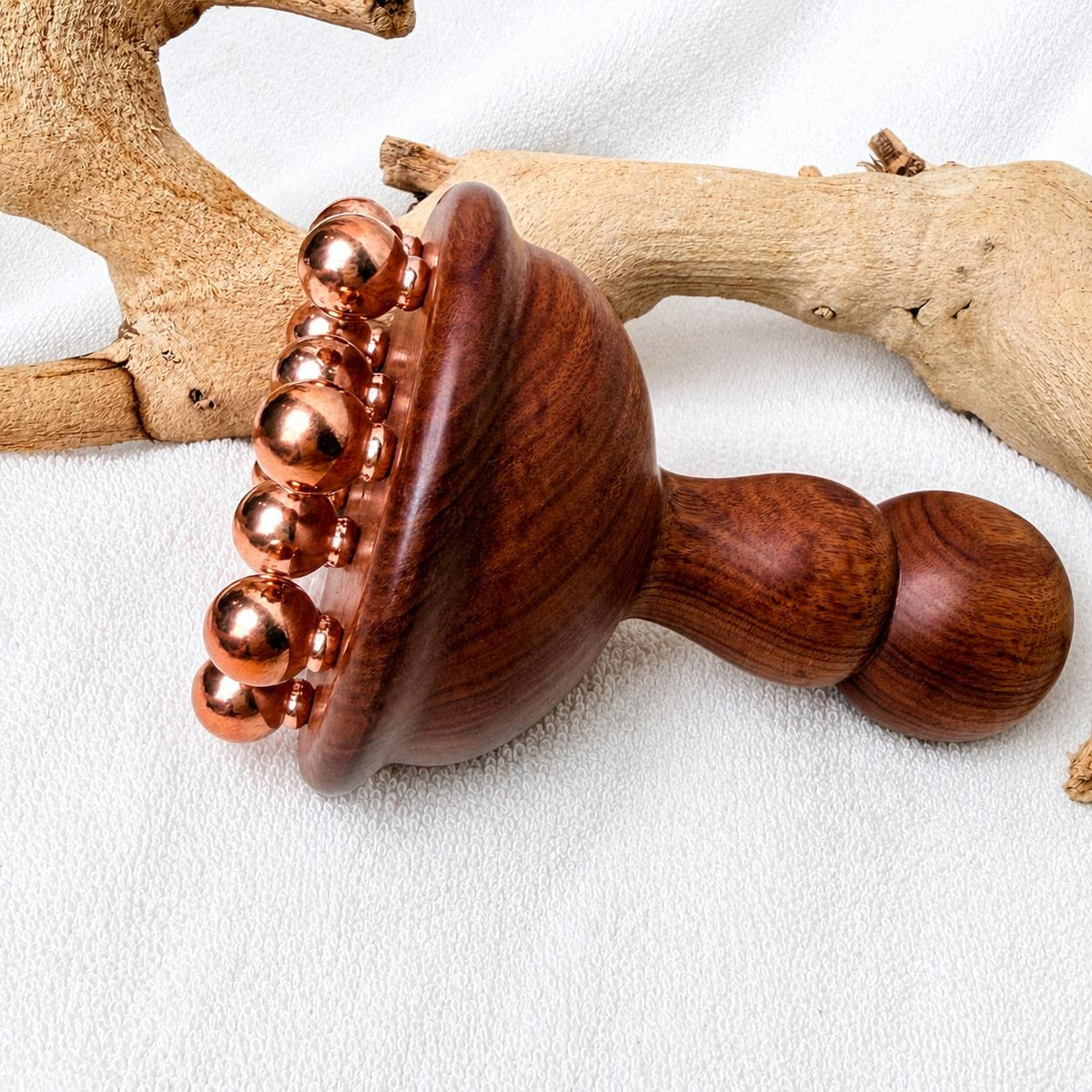 Close-up detail of the copper and rosewood body contouring massage tool on driftwood