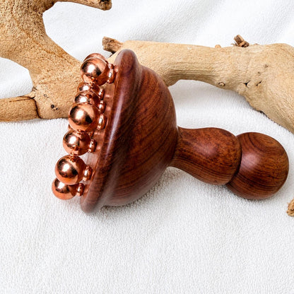 Close-up detail of the copper and rosewood body contouring massage tool on driftwood