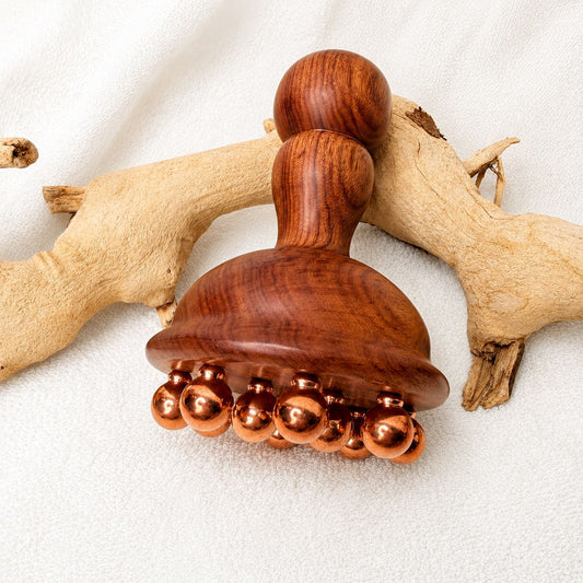 Copper and rosewood body contouring massage tool displayed on driftwood