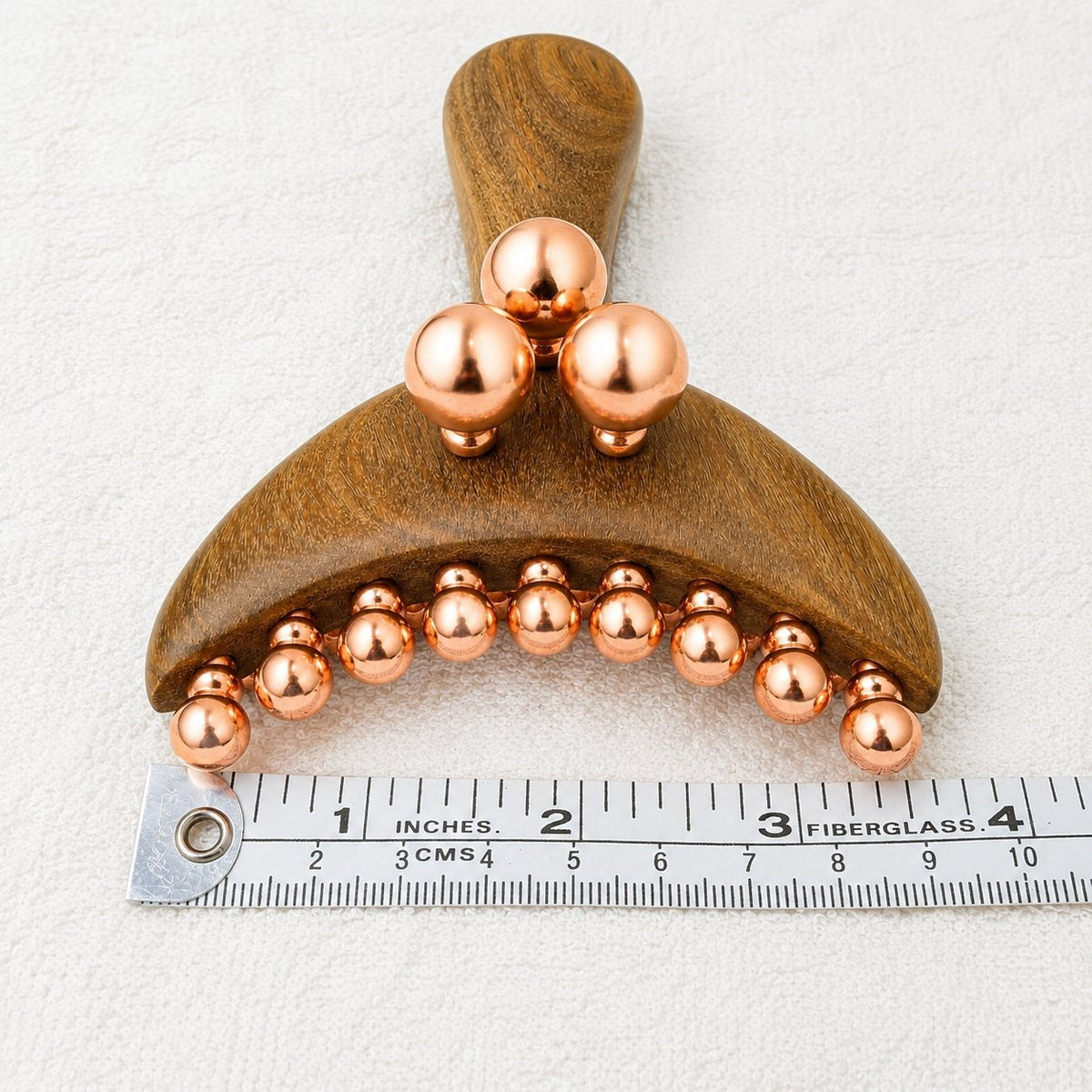 Front view of the Copper & Wood Deep Tissue Massage Tool next to a ruler showing its width, with the curved row of copper balls and three raised balls above the handle
