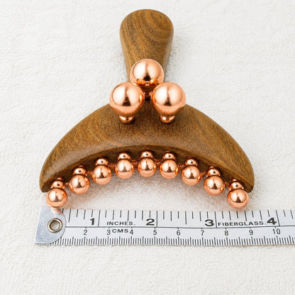 Front view of the Copper & Wood Deep Tissue Massage Tool next to a ruler showing its width, with the curved row of copper balls and three raised balls above the handle