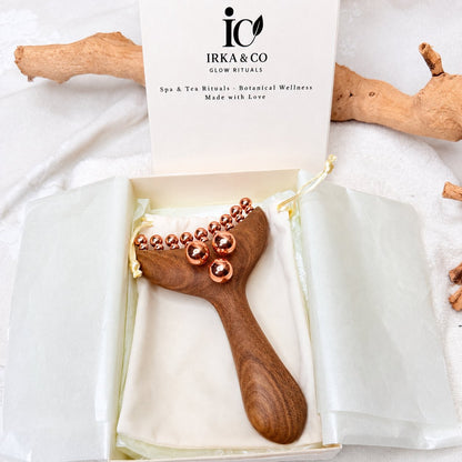 Copper & Wood Deep Tissue Massage Tool nestled in an open IRKA & CO gift box on a cream pouch, styled with driftwood and a branded card
