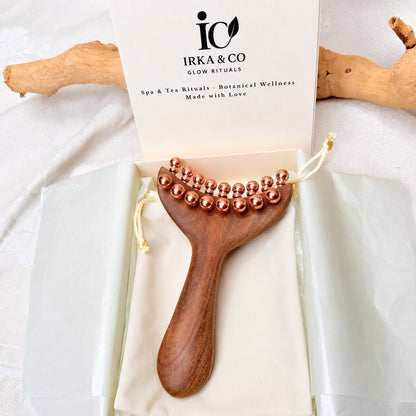 Copper & Wood Deep Tissue Massage Tool in its open IRKA & CO gift box with the Glow Rituals branded insert card, driftwood in the background