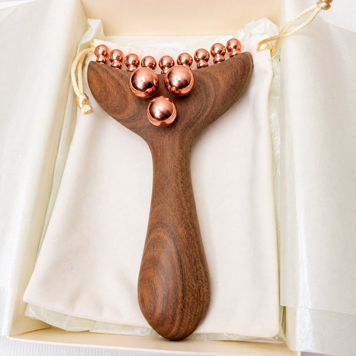Copper & Wood Deep Tissue Massage Tool lying in its gift box on a cotton pouch, showing the triple copper-ball cluster near the handle and the curved bead row