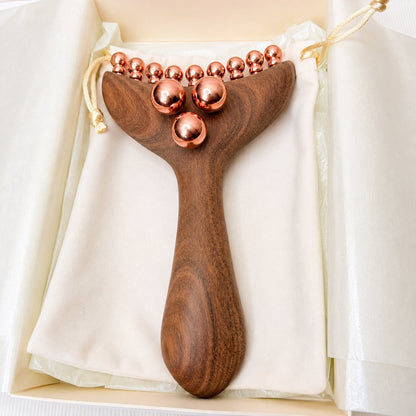 Copper & Wood Deep Tissue Massage Tool lying in its gift box on a cotton pouch, showing the triple copper-ball cluster near the handle and the curved bead row