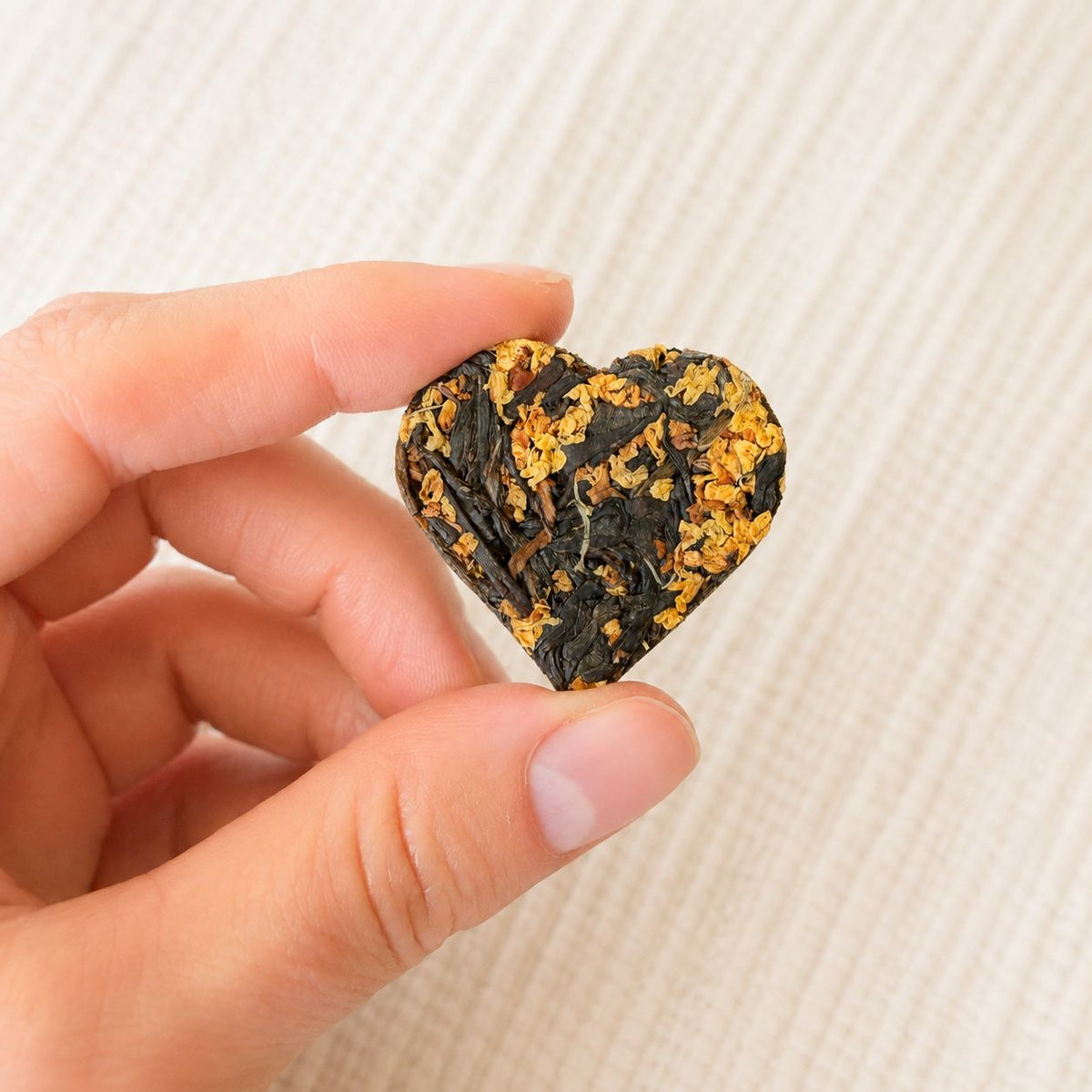 Close-up of a single compressed tea heart with osmanthus blossoms held between two fingers