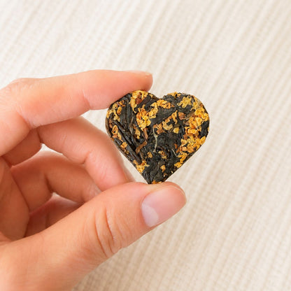 Close-up of a single compressed tea heart with osmanthus blossoms held between two fingers