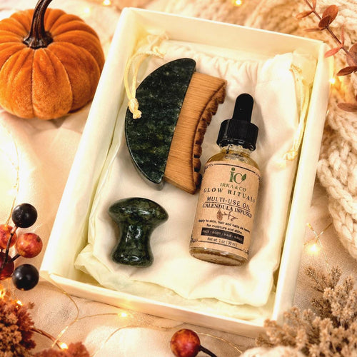 Jade Ritual Set with gua sha, wooden comb, mushroom roller, and Calendula Infused Multi-Use Oil in an open IRKA & CO gift box styled with autumn decor