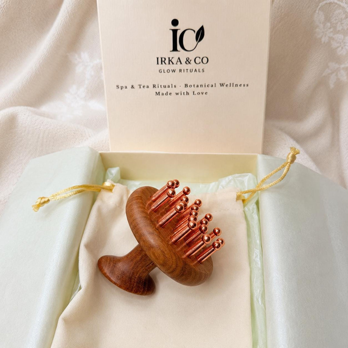 Copper & Sandalwood Scalp Massage Comb in its open IRKA & CO gift box on a cream pouch with the Glow Rituals branded card