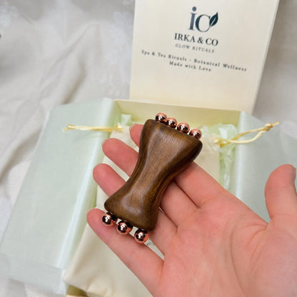 Copper & Sandalwood Facial Massage Tool resting in an open palm with the IRKA & CO Glow Rituals gift box and branded card in the background